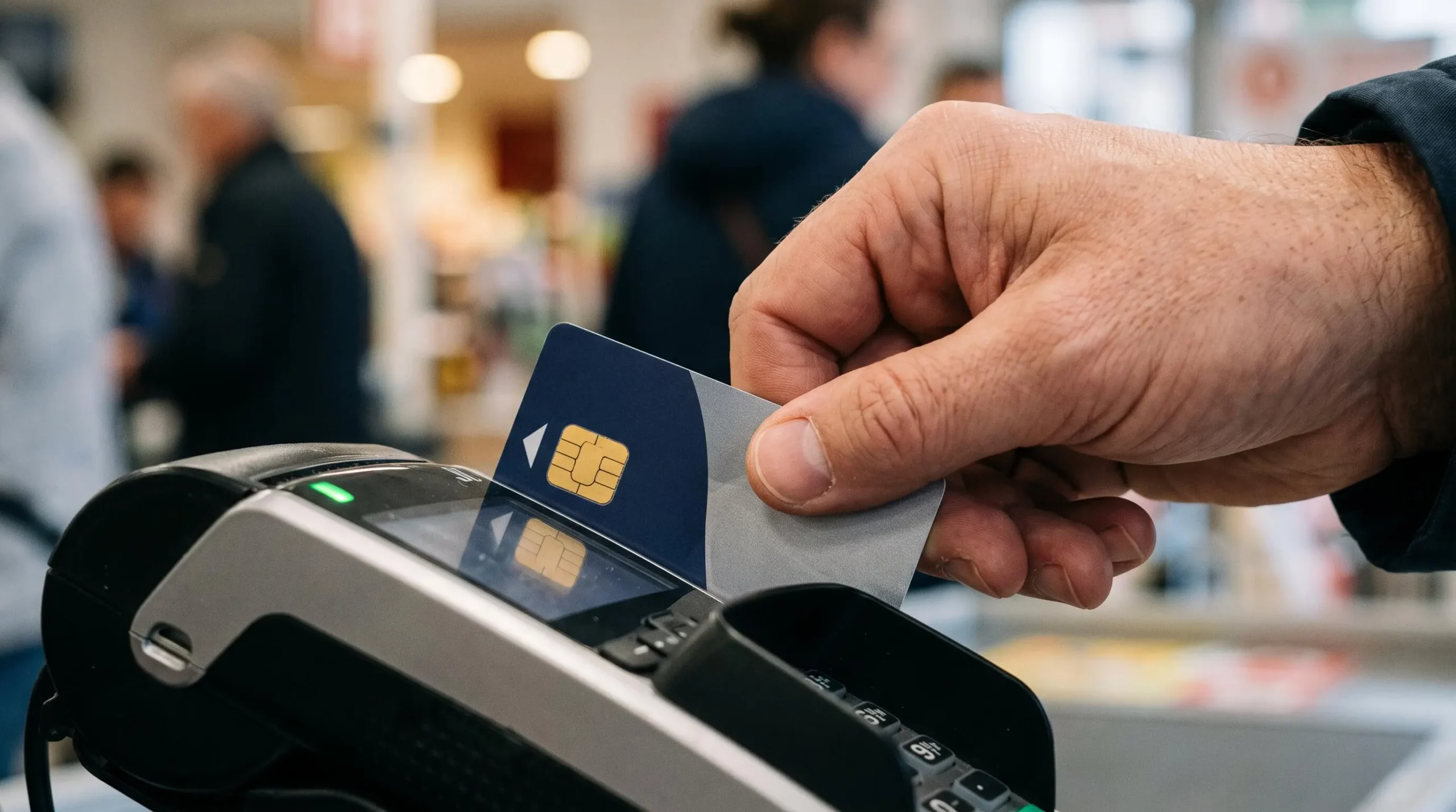 Main tenant une carte bancaire devant un terminal de paiement lors d'une transaction quotidienne.